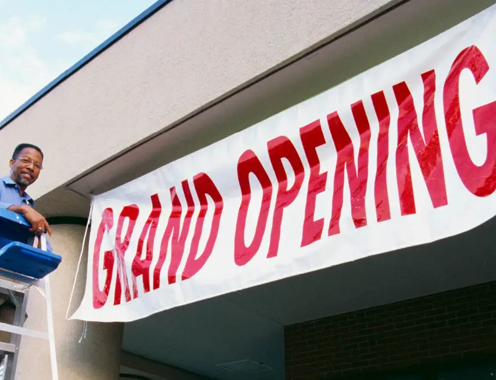 Man on ladder putting up a Grand Opening sign