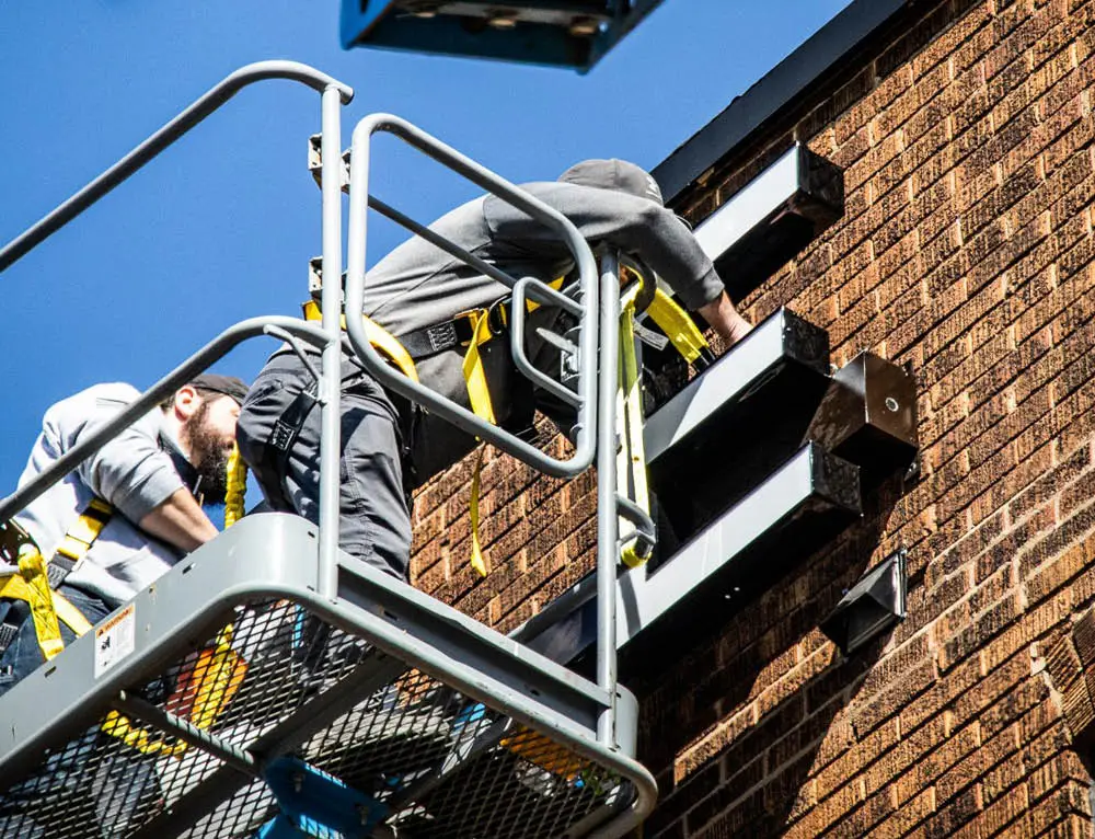 A crew on a crane installs a sign on a brick building