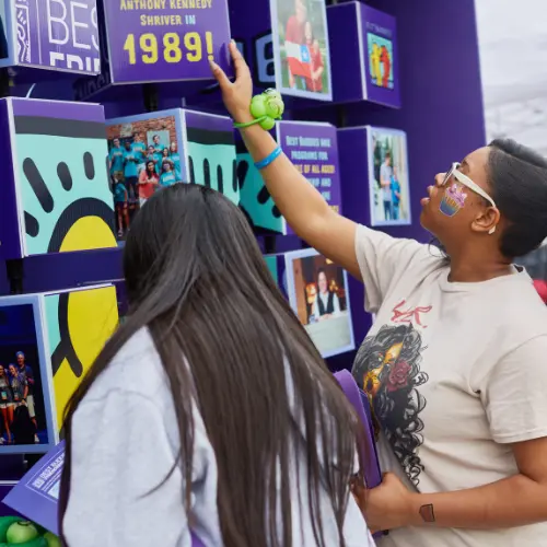 Two girls spin cubes on a cube wall containing facts on each side of the cubes.
