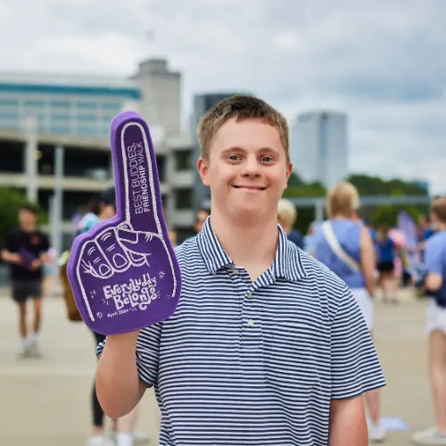 A young man wears a purple Best Buddies finger and points it in the air