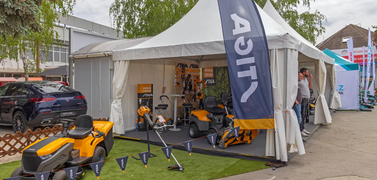 Tent with surrounded by mowers with branded feather flags, decorative flags, and banners