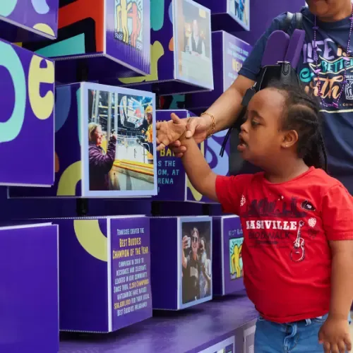 A young girl and woman turn cubes that are part of a large display of cubes with graphics and facts about Best Buddies on each side