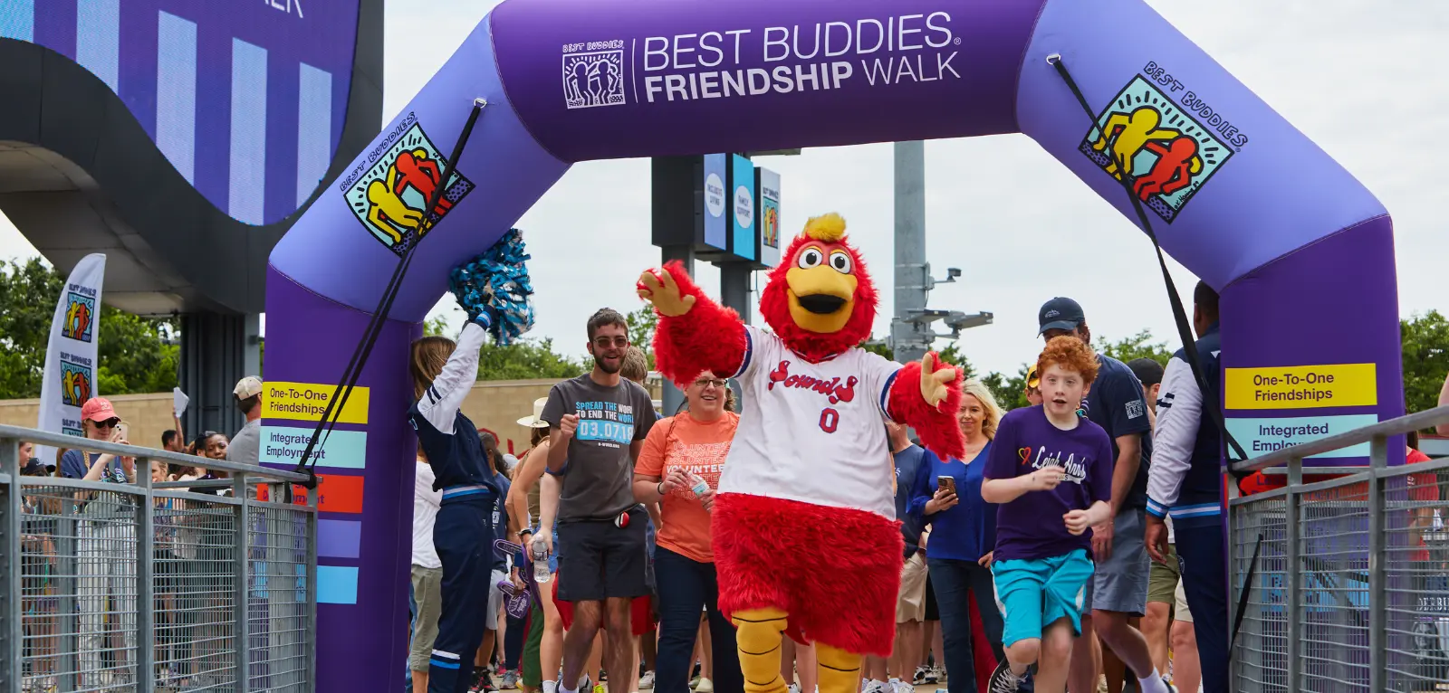 Walkers and a mascot run through a large inflatable Best Buddies arch
