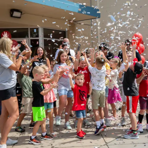 A group of students and adults celebrate with confetti outside of a school