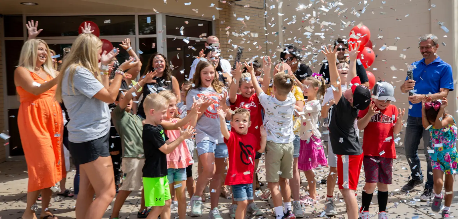 A group of students and adults celebrate outside of a school with confetti