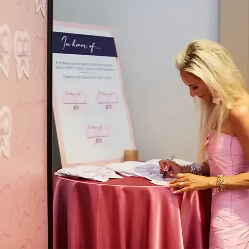  A woman writes on a paper bow next to a wall with bows containing written donation pledges