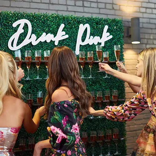 Women take glasses of champagne from a champagne wall with the words 