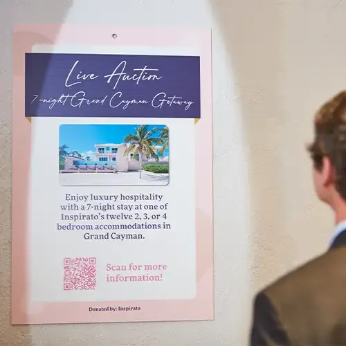 Man looks at poster on wall with details on live auction item, 7-Night Grand Cayman Getaway.
