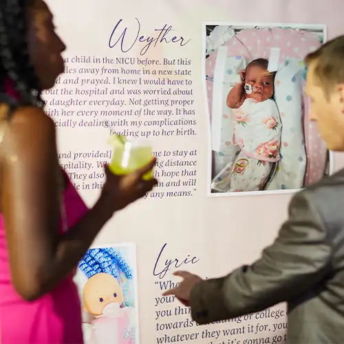 People pointing at a sign with photos, names, and stories of NICU babies