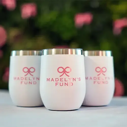 White tumblers with the Madelyn's Fund logo which is their name and a bow, all in pink.