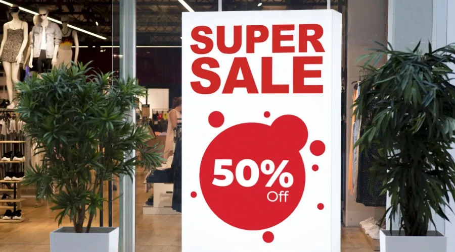 White and red super sale sign in front of a store between two plants